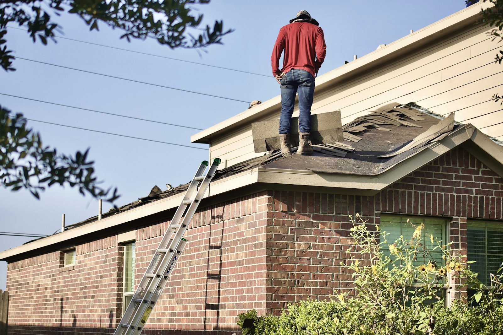 Roofing worker removing old shingles from a house roof
